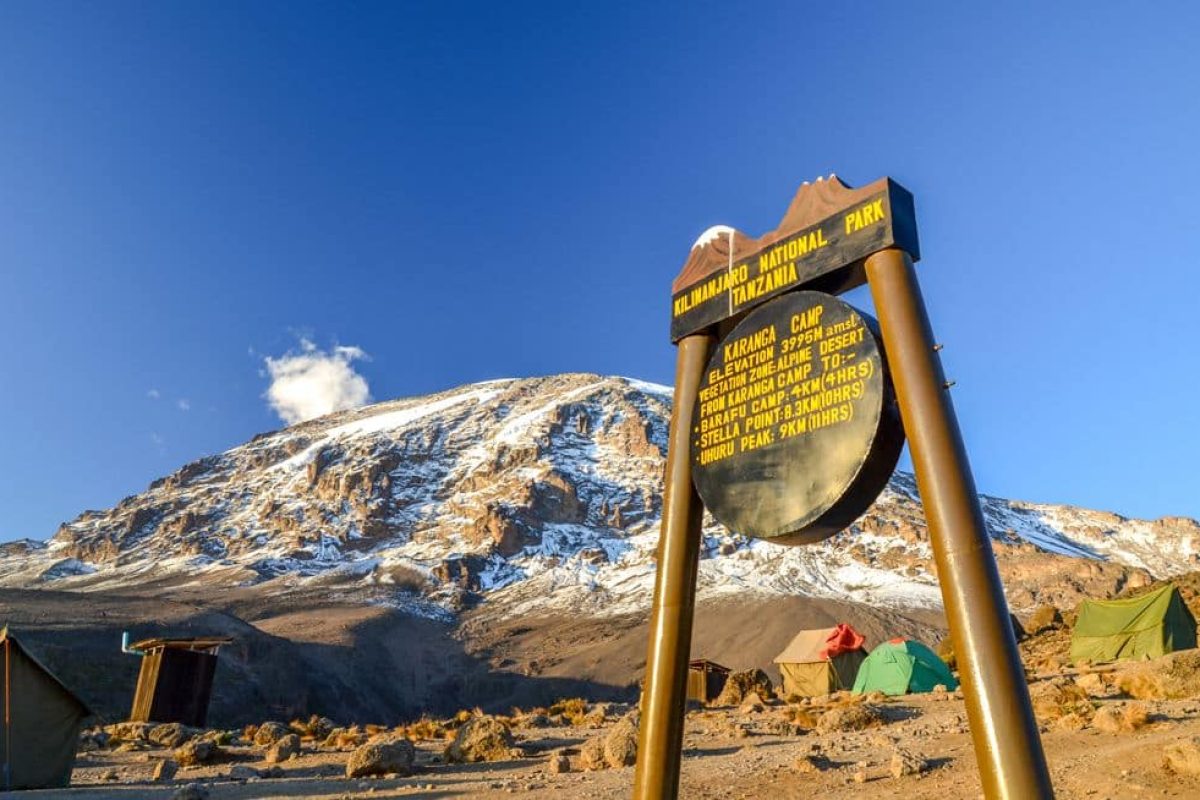 Kilimanjaro, Tanzania - March 9, 2015: Kibo with Uhuru Peak (5895m amsl) at Mount Kilimanjaro, Kilimanjaro National Park, seen from Karanga Camp at 3995m amsl. Park sign and tents in the background.
